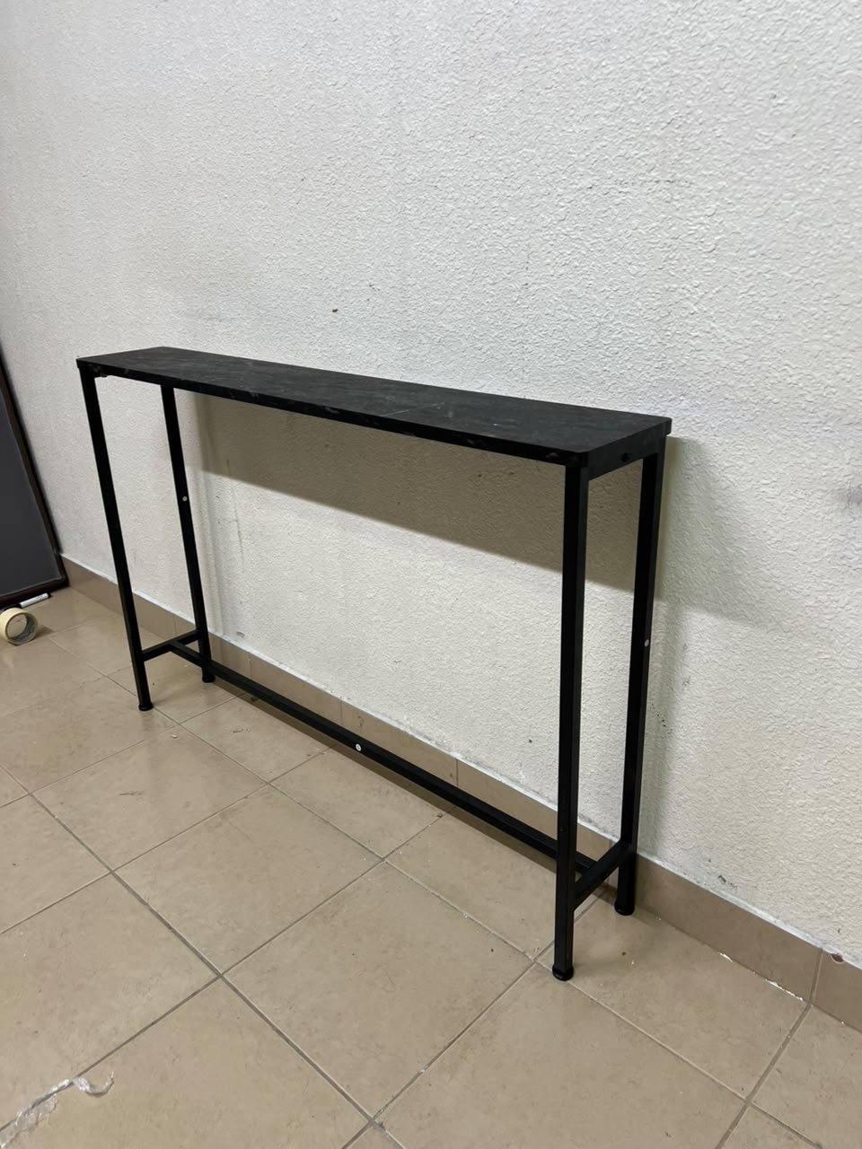 A console or sofa table—narrow and sleek—featuring a black metal frame and a rectangular top.