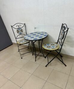 A three-piece black wrought-iron table and chair set, featuring blue and yellow ceramic mosaic tile accents on the round tabletop and the seats of the foldable chairs. - Image 3