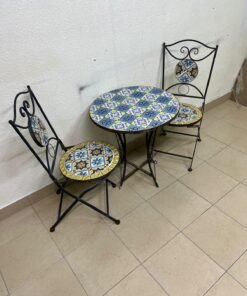 A three-piece black wrought-iron table and chair set, featuring blue and yellow ceramic mosaic tile accents on the round tabletop and the seats of the foldable chairs.