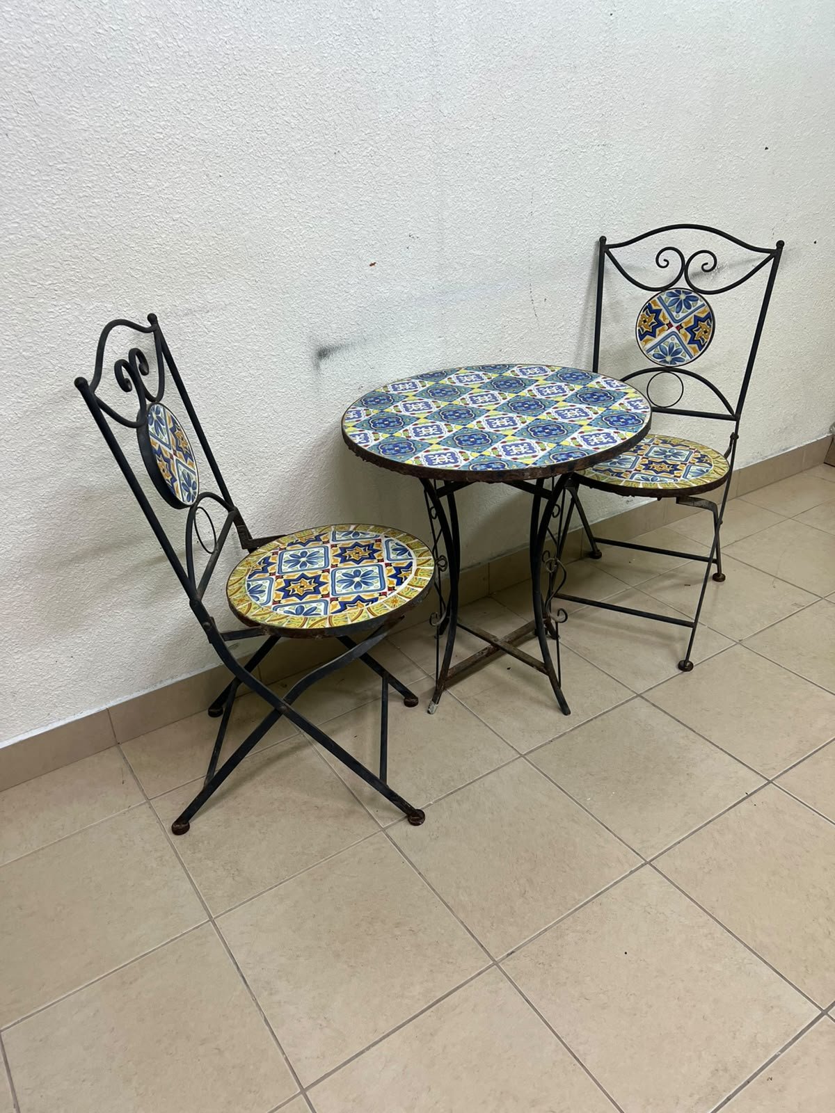 A three-piece black wrought-iron table and chair set, featuring blue and yellow ceramic mosaic tile accents on the round tabletop and the seats of the foldable chairs. - Image 7