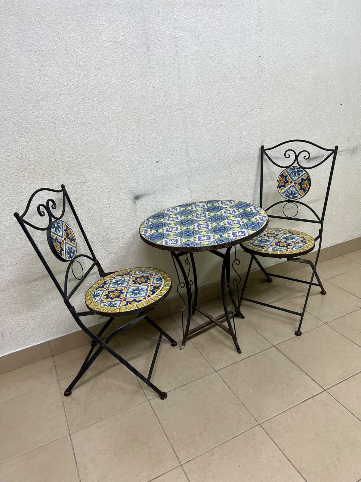 A three-piece black wrought-iron table and chair set, featuring blue and yellow ceramic mosaic tile accents on the round tabletop and the seats of the foldable chairs. - Image 8