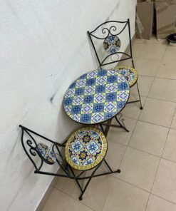 A three-piece black wrought-iron table and chair set, featuring blue and yellow ceramic mosaic tile accents on the round tabletop and the seats of the foldable chairs. - Image 9