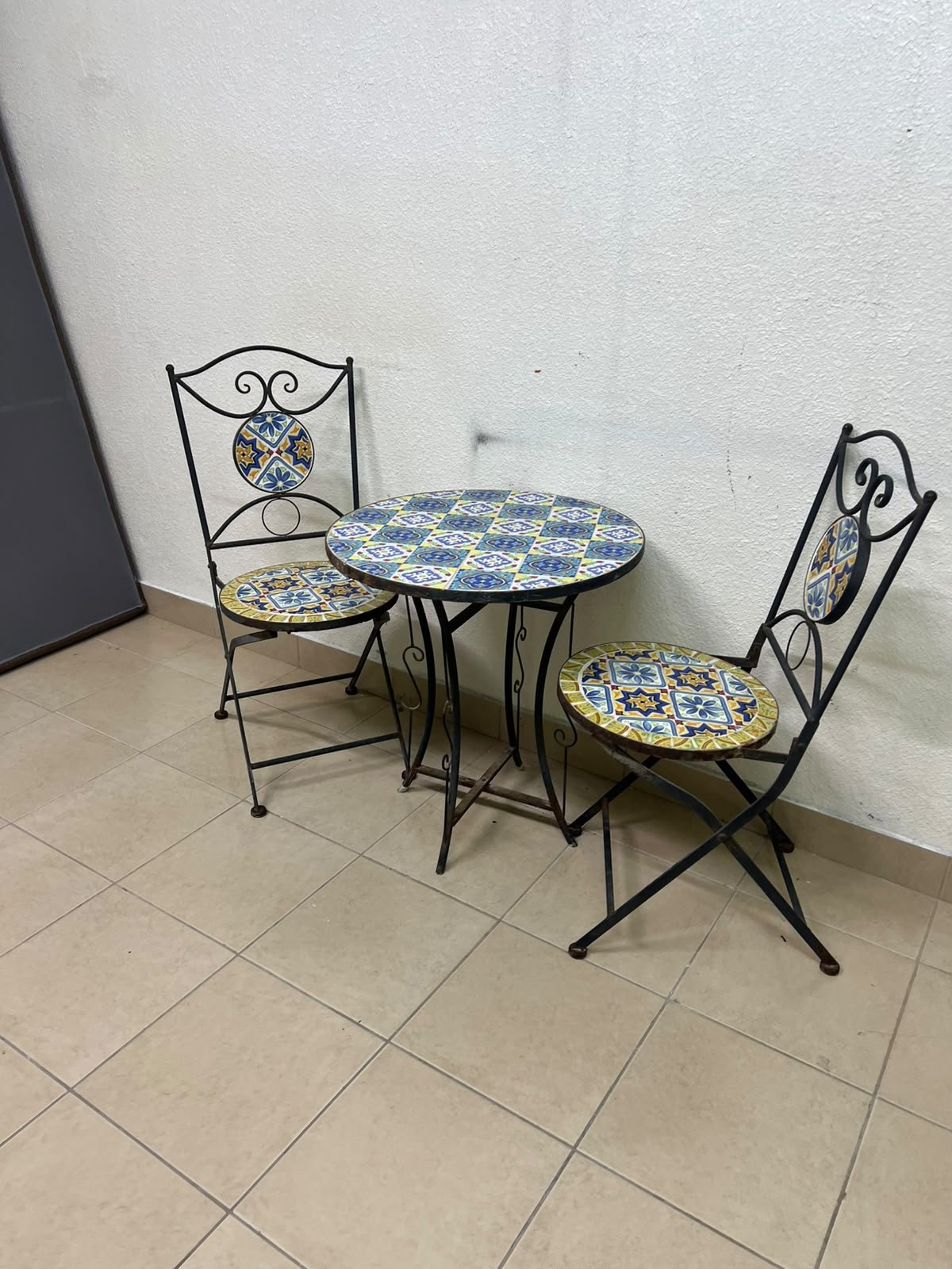 A three-piece black wrought-iron table and chair set, featuring blue and yellow ceramic mosaic tile accents on the round tabletop and the seats of the foldable chairs. - Image 10