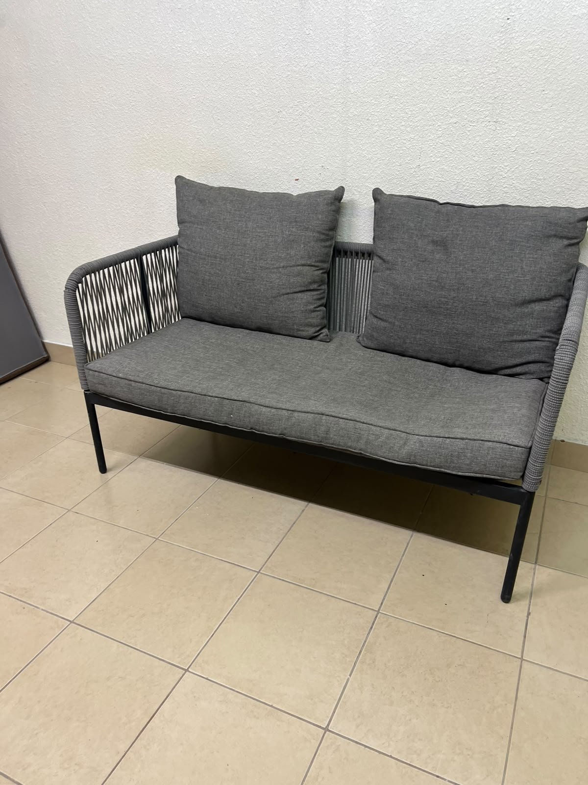 The two-seater outdoor sofa is a modern piece featuring a grey rope-woven design, a black metal frame, and matching back cushions.