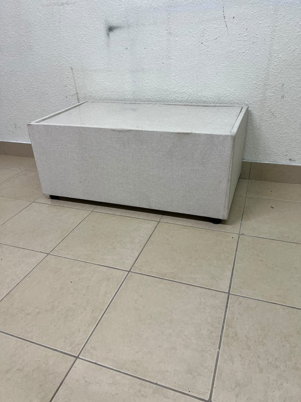 A coffee table upholstered in beige fabric with a textured feel and a neutral, linen-like appearance.