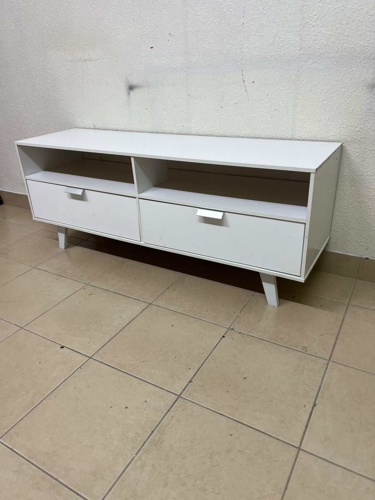 A modern, white, freestanding TV stand featuring angled legs and two large lower storage drawers, topped by open shelves. - Image 8