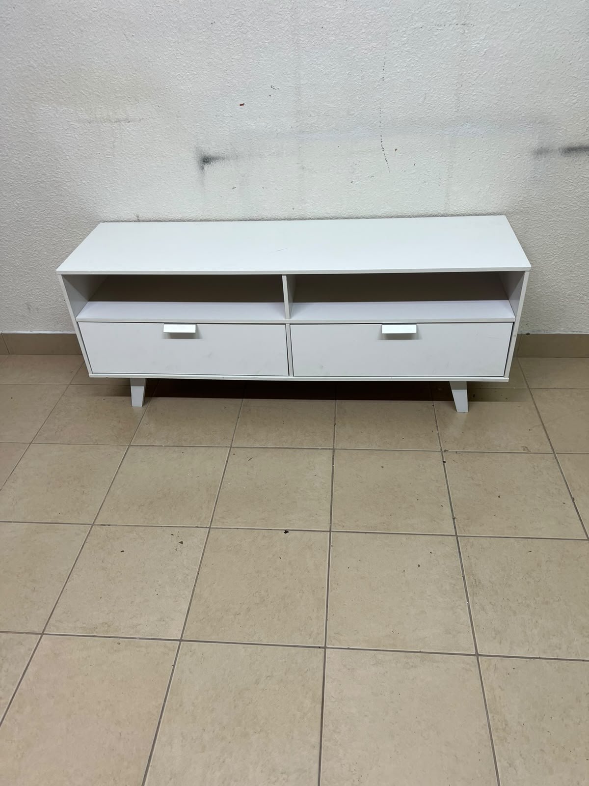A modern, white, freestanding TV stand featuring angled legs and two large lower storage drawers, topped by open shelves. - Image 9