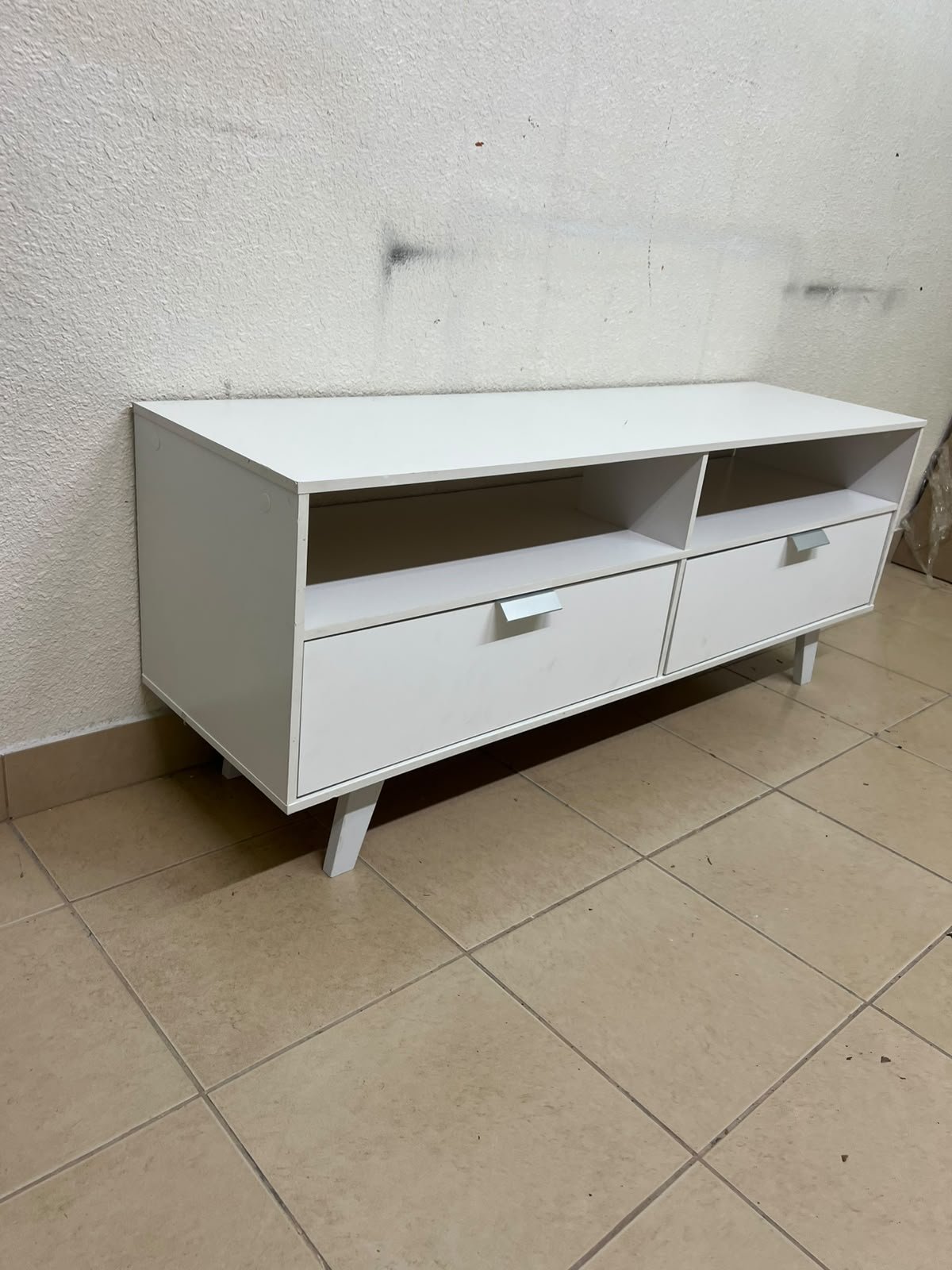 A modern, white, freestanding TV stand featuring angled legs and two large lower storage drawers, topped by open shelves. - Image 4