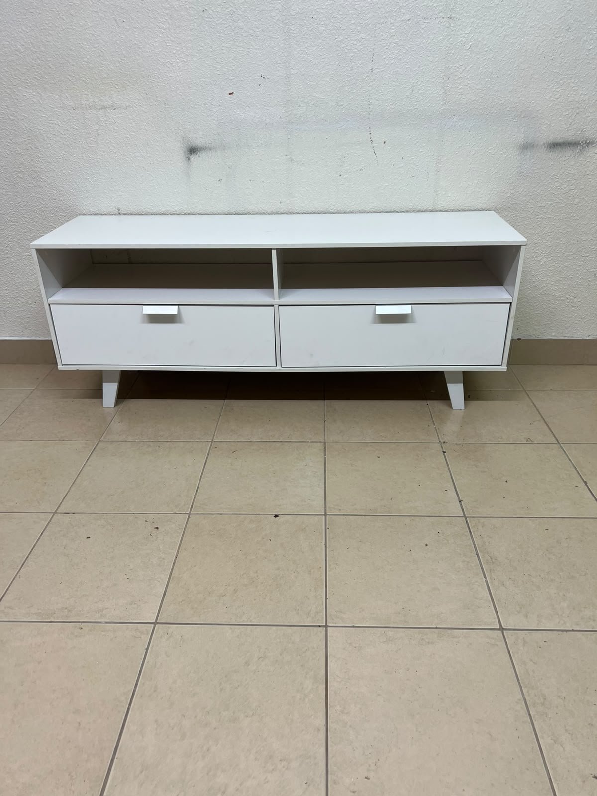 A modern, white, freestanding TV stand featuring angled legs and two large lower storage drawers, topped by open shelves. - Image 3