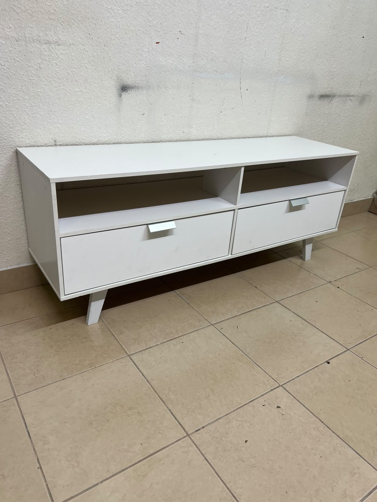 A modern, white, freestanding TV stand featuring angled legs and two large lower storage drawers, topped by open shelves. - Image 2