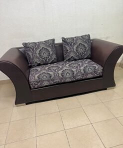 The sofa is designed for two people and upholstered in dark brown faux leather, with a purple and gray damask-patterned fabric covering the seat cushions and matching throw pillows. - Image 2