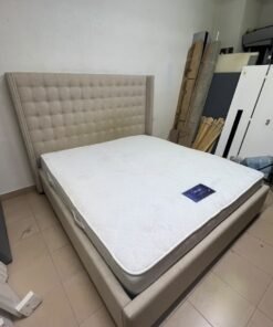 A beige, winged, upholstered bed featuring a button-tufted headboard and nailhead trim.