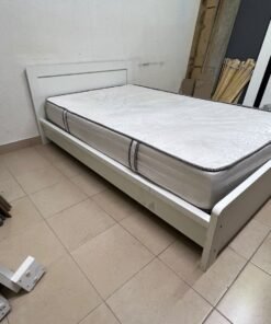 The image shows a white wooden bed frame with a matching headboard and a patterned mattress.