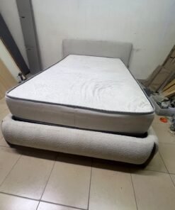 A modern, curved bed frame upholstered in off-white bouclé fabric with dark wood accents, complemented by a patterned, cushioned mattress. - Image 2
