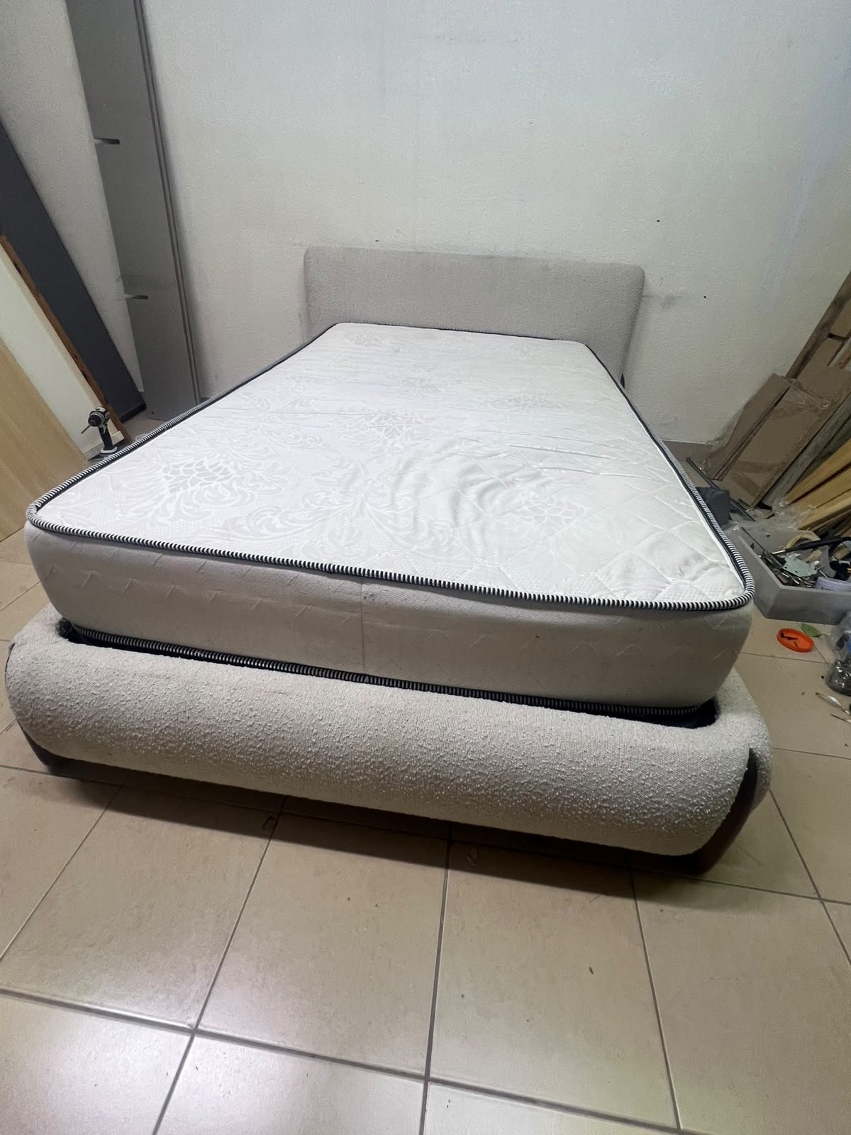 A modern, curved bed frame upholstered in off-white bouclé fabric with dark wood accents, complemented by a patterned, cushioned mattress. - Image 2