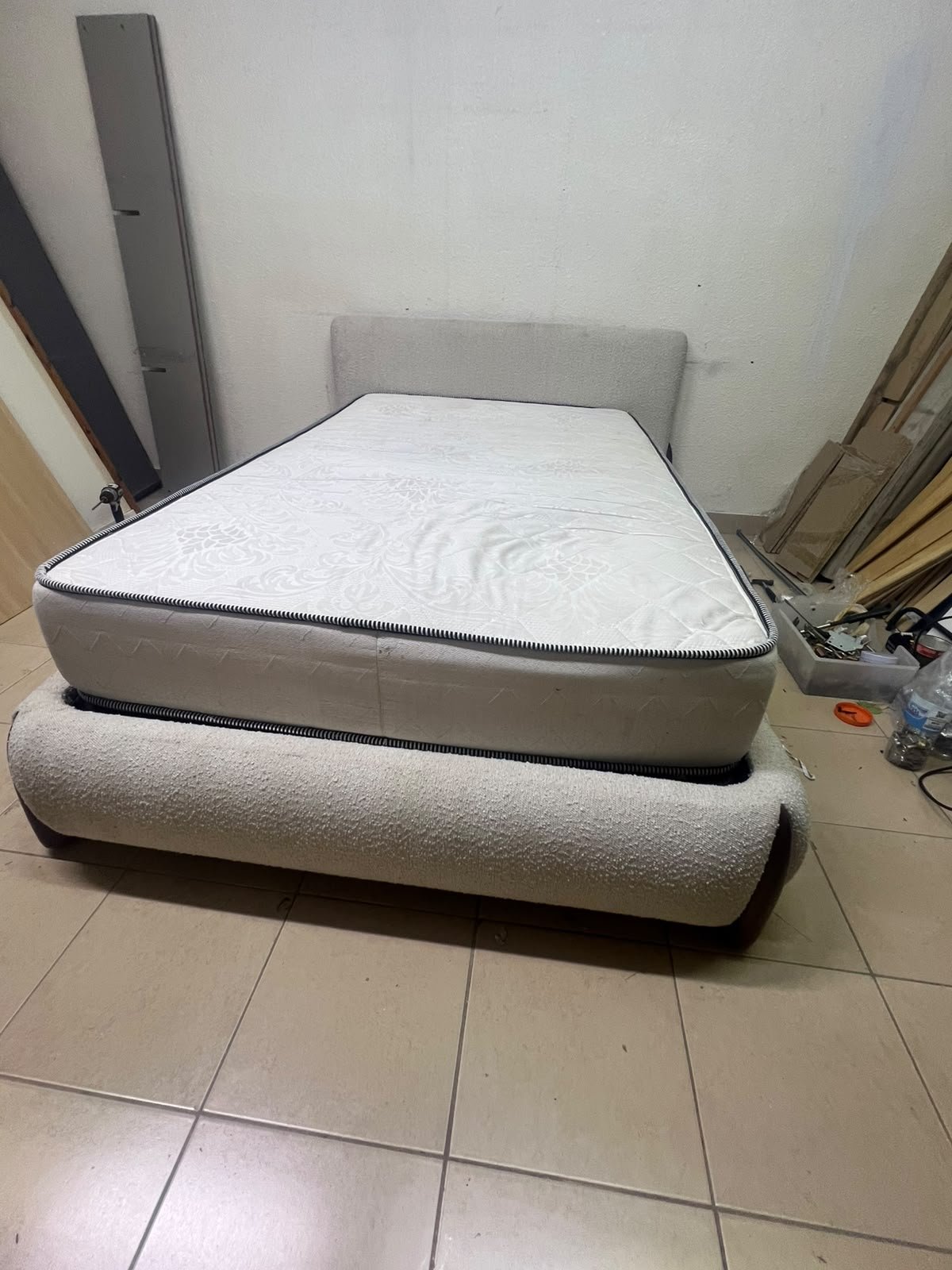 A modern, curved bed frame upholstered in off-white bouclé fabric with dark wood accents, complemented by a patterned, cushioned mattress. - Image 4
