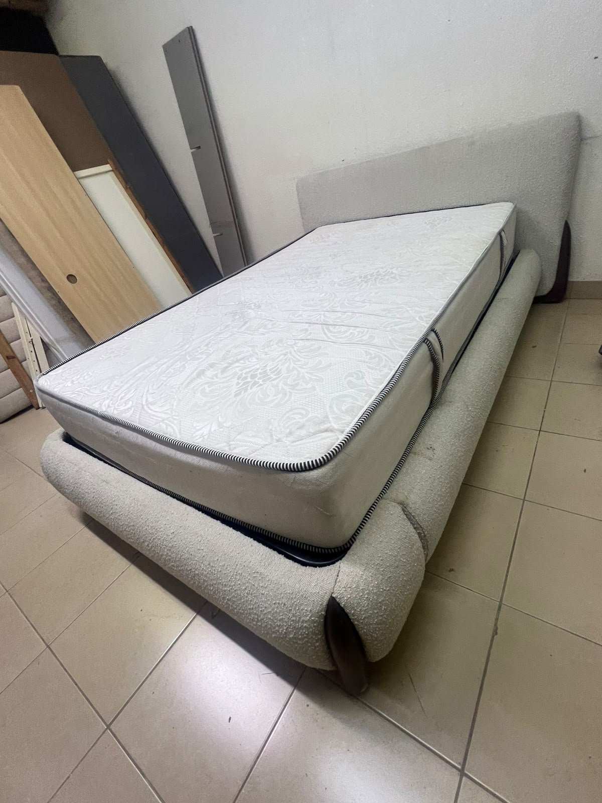 A modern, curved bed frame upholstered in off-white bouclé fabric with dark wood accents, complemented by a patterned, cushioned mattress. - Image 5