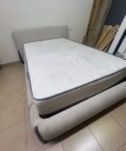 A modern, curved bed frame upholstered in off-white bouclé fabric with dark wood accents, complemented by a patterned, cushioned mattress. - Image 8