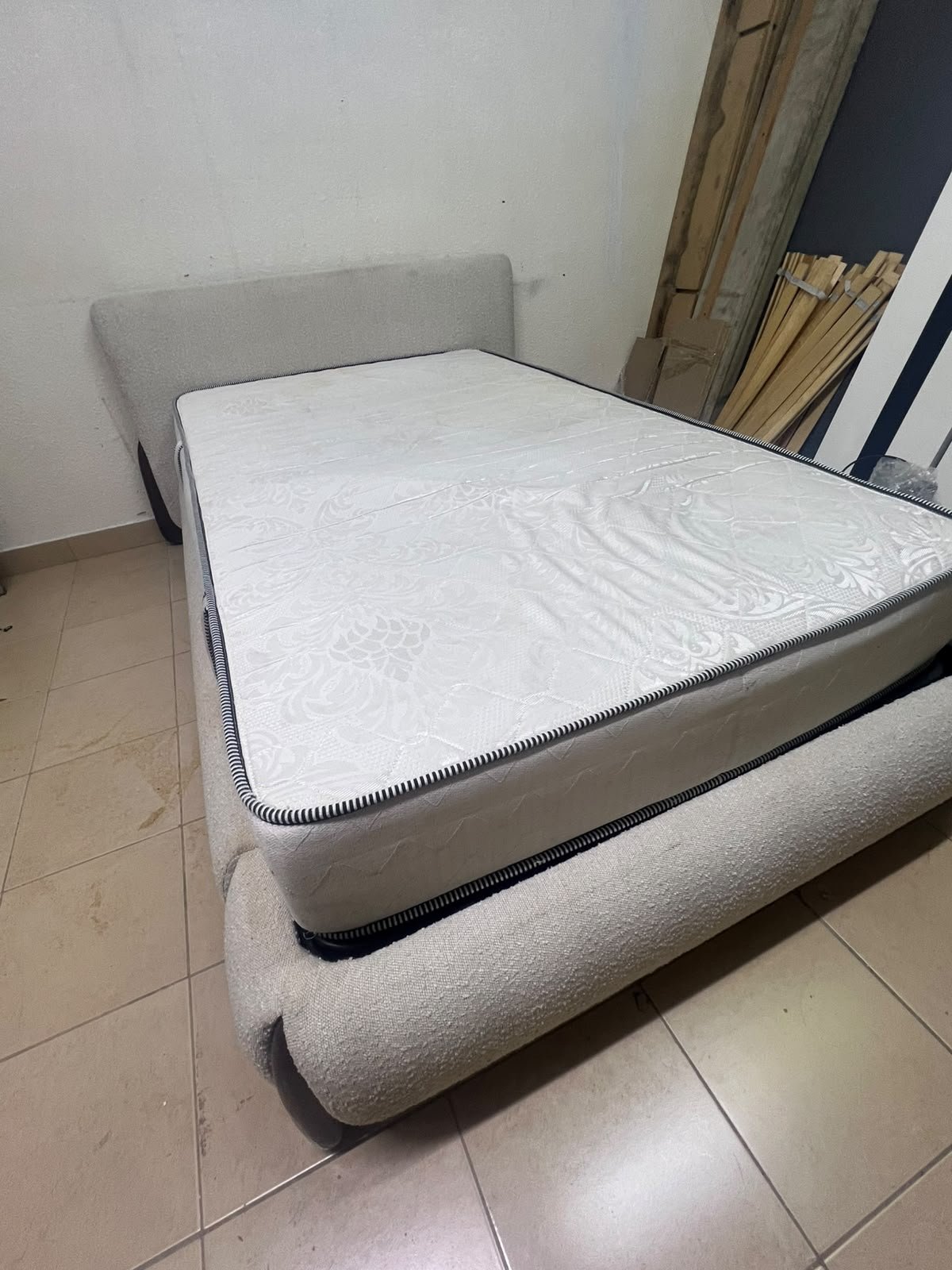 A modern, curved bed frame upholstered in off-white bouclé fabric with dark wood accents, complemented by a patterned, cushioned mattress. - Image 8