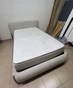 A modern, curved bed frame upholstered in off-white bouclé fabric with dark wood accents, complemented by a patterned, cushioned mattress. - Image 10
