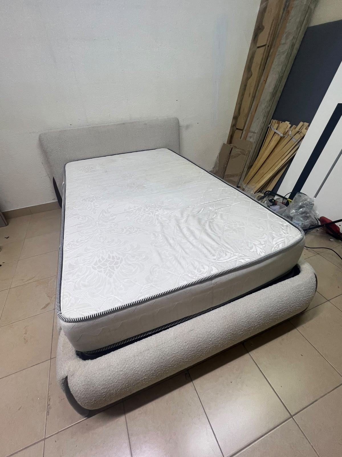 A modern, curved bed frame upholstered in off-white bouclé fabric with dark wood accents, complemented by a patterned, cushioned mattress. - Image 10