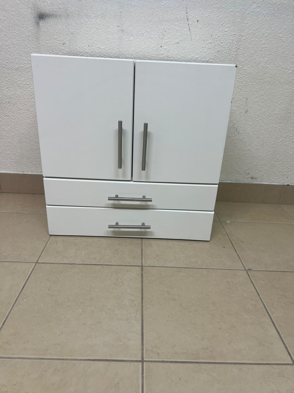 A white wooden storage cabinet featuring two upper doors and two lower drawers equipped with rectangular silver handles.