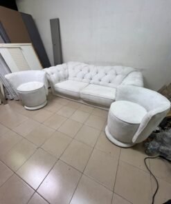 A modern living room furniture set in an off-white or cream hue, featuring a cushioned sofa with a curved back, complemented by matching barrel-style swivel chairs with round bases.