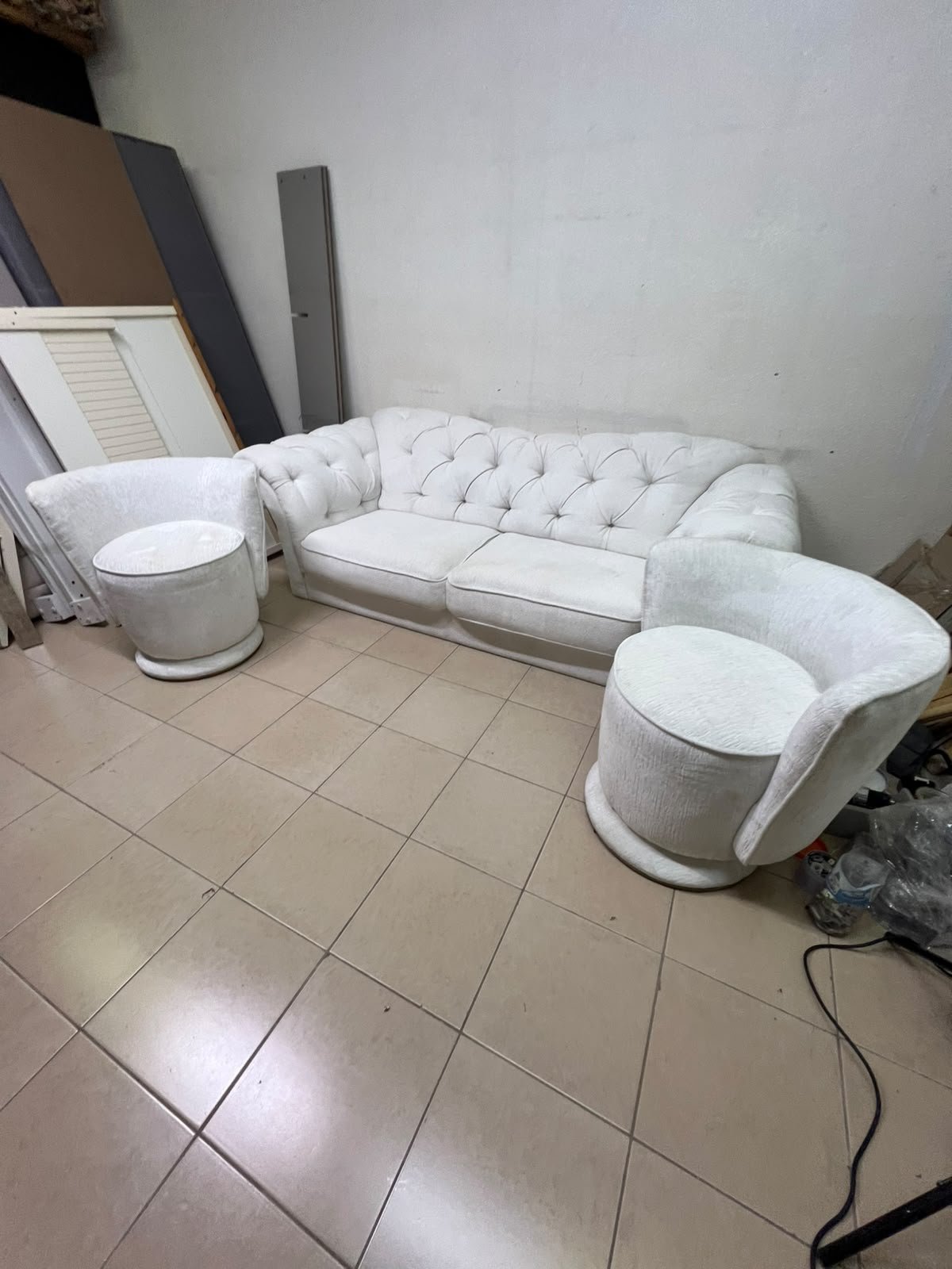 A modern living room furniture set in an off-white or cream hue, featuring a cushioned sofa with a curved back, complemented by matching barrel-style swivel chairs with round bases.