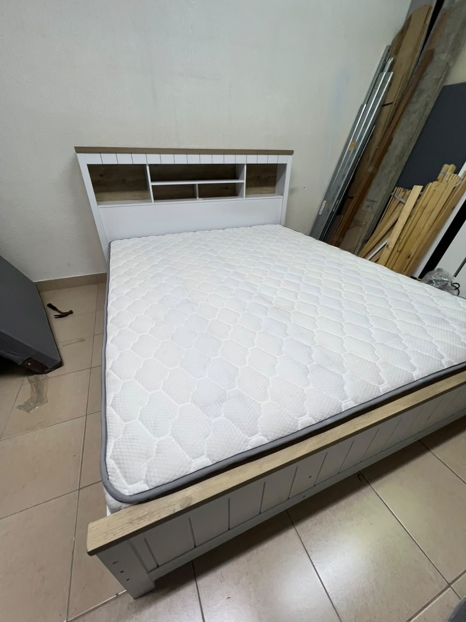 A white wooden King-size bed frame featuring an integrated headboard with shelves, accompanied by a matching padded mattress.