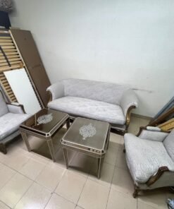 A light-colored, upholstered classic living room set featuring a sofa and armchairs with carved wooden frames, along with two matching mirrored side tables.