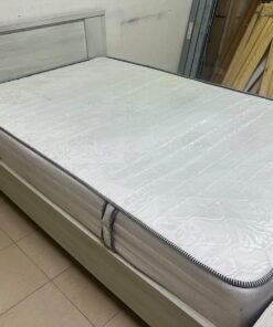 A double bed with a light wood finish, featuring a paneled headboard and a standard upholstered mattress.