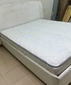 A modern, minimalist beige platform bed featuring a curved, upholstered headboard and a cushioned white mattress.
