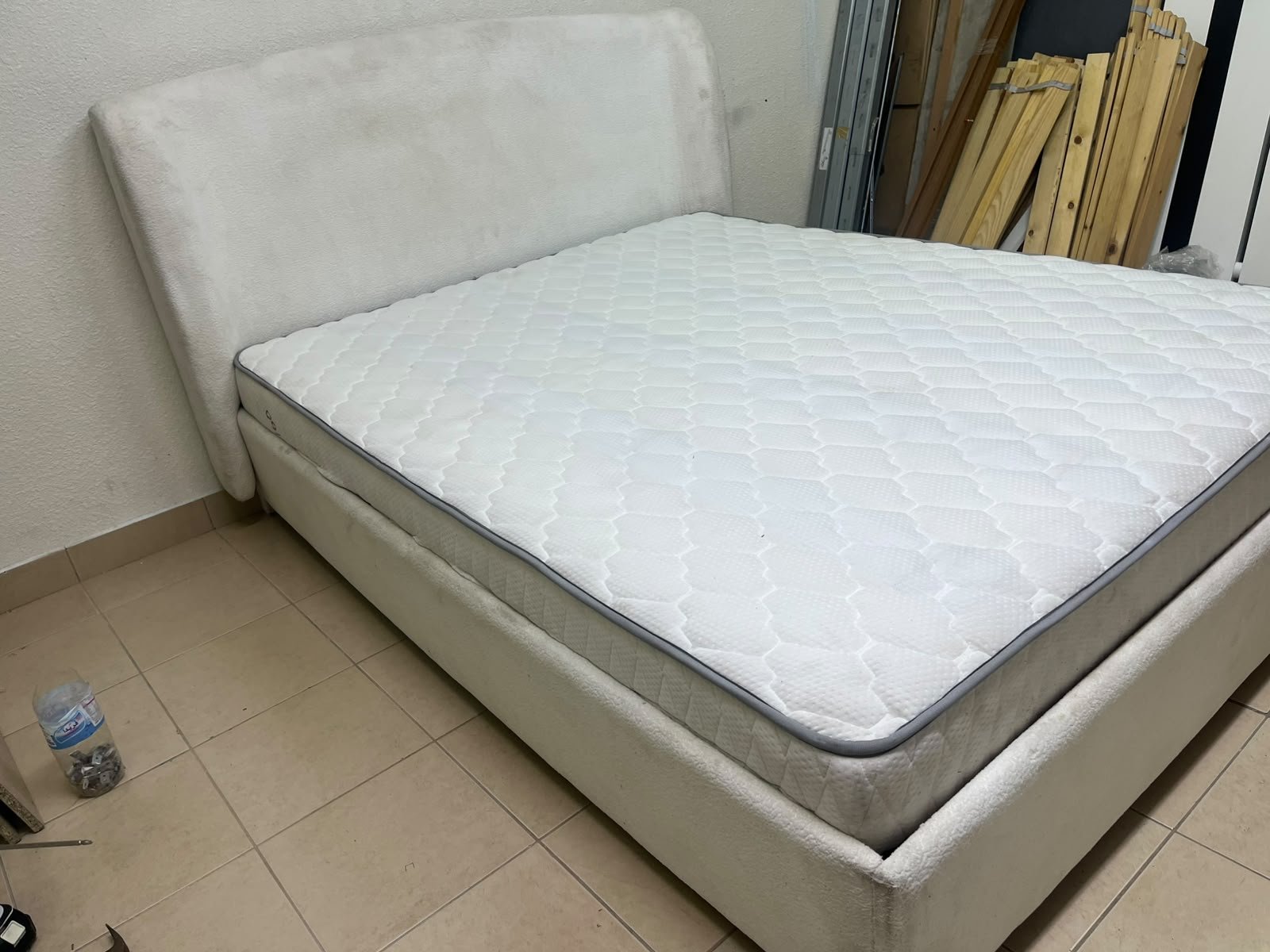 A modern, minimalist beige platform bed featuring a curved, upholstered headboard and a cushioned white mattress.