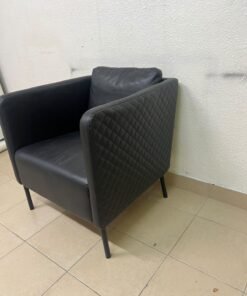 The IKEA EKERÖ armchair, upholstered in black Bomstad material, featuring distinctive slender black legs and a loose back cushion.
