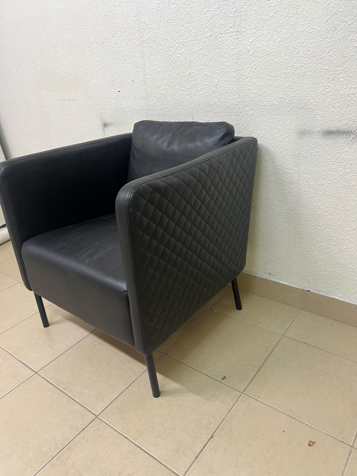 The IKEA EKERÖ armchair, upholstered in black Bomstad material, featuring distinctive slender black legs and a loose back cushion.