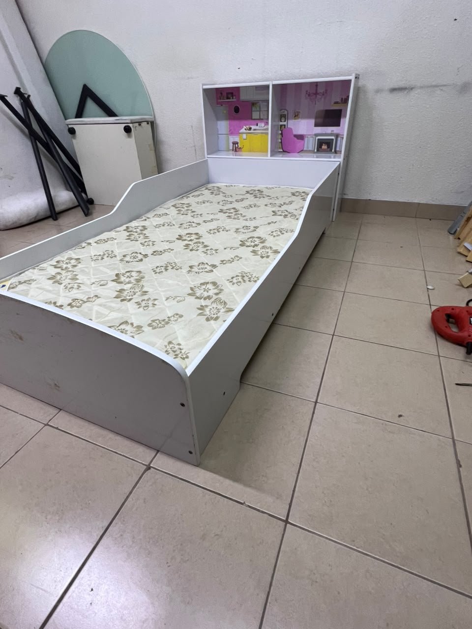A white wooden single bed for children, featuring an integrated "dollhouse-style" headboard decorated with illustrations of miniature rooms.