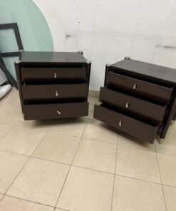 A pair of modern dark-wood bedside cabinets featuring three drawers, curved fronts, silver-colored handles, and elegant metal legs.
