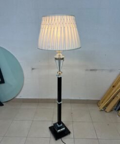An elegant floor lamp combining crystal and black metal, featuring a conical, pleated fabric shade and a multi-faceted glass element positioned near the top of the lamp's stem.