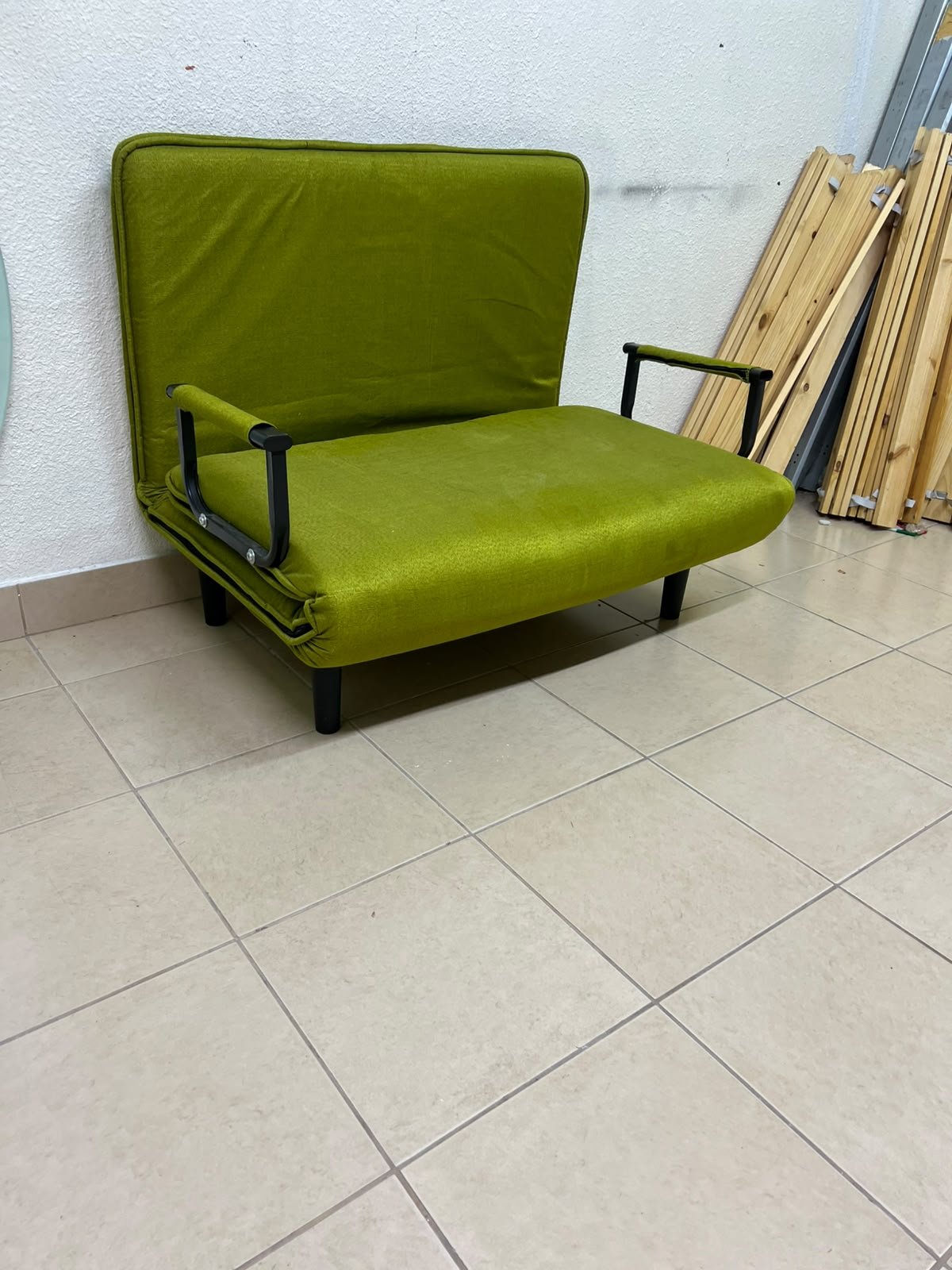 A multifunctional, foldable green sofa bed featuring black metal armrests and an adjustable backrest.