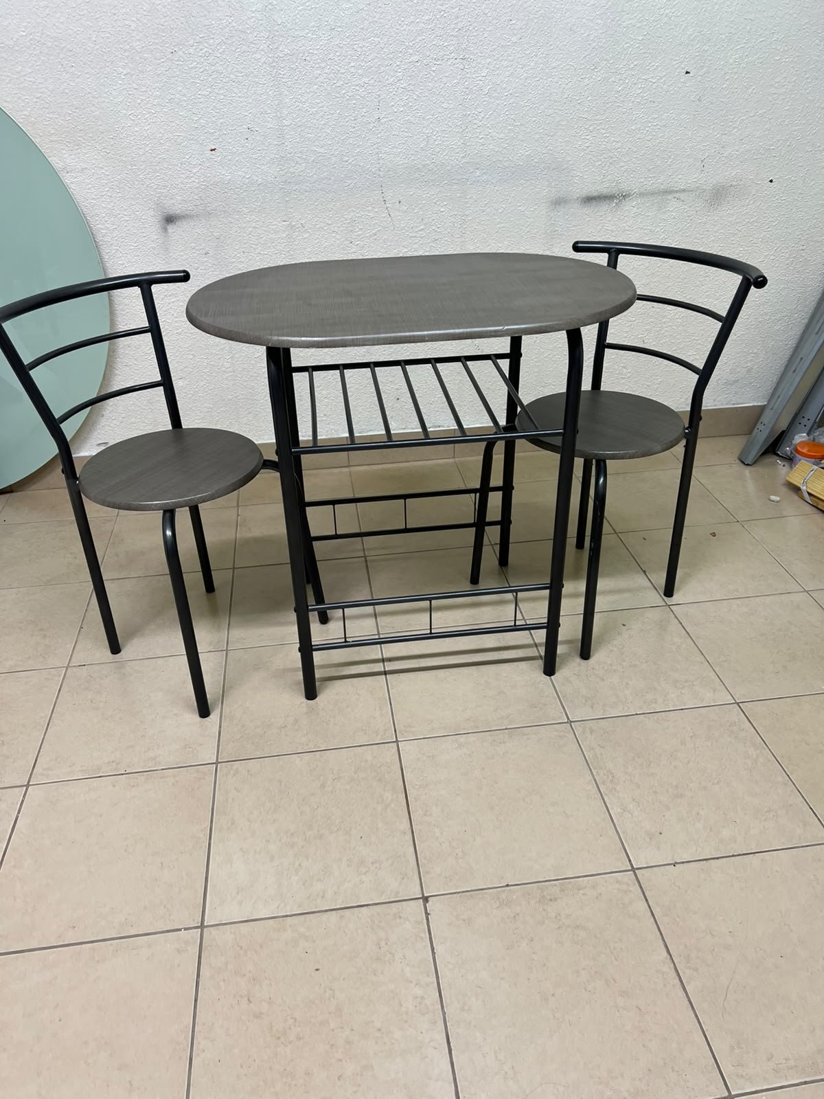 Two chairs and a table featuring an oval grey tabletop, a black tubular steel frame, and built-in storage shelves. - Image 2
