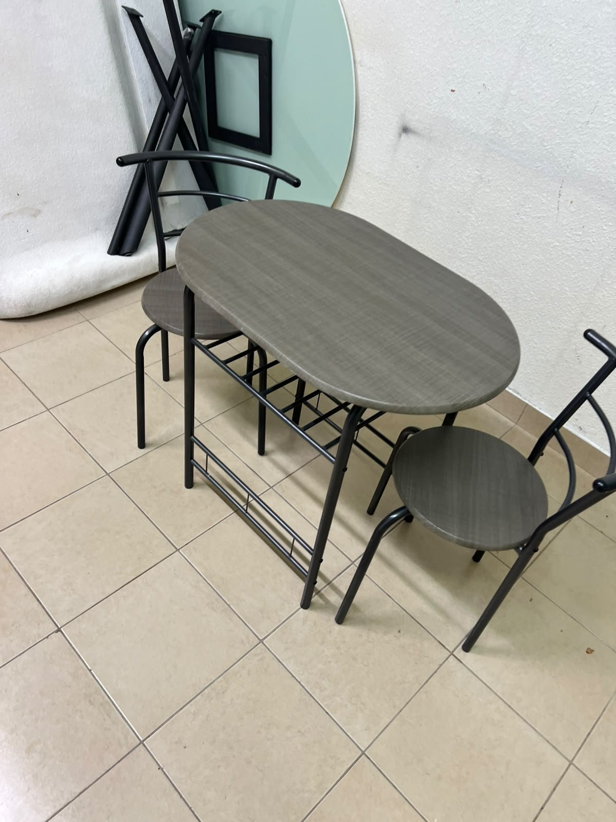 Two chairs and a table featuring an oval grey tabletop, a black tubular steel frame, and built-in storage shelves. - Image 3