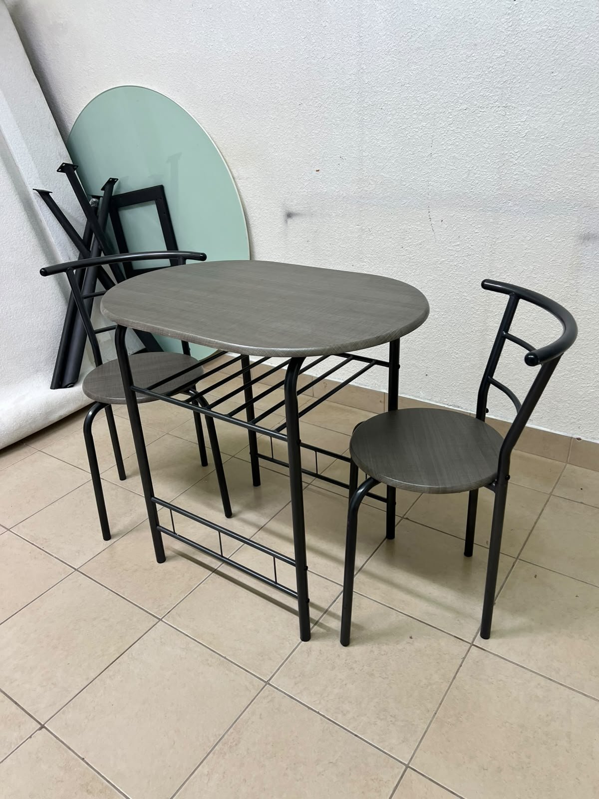 Two chairs and a table featuring an oval grey tabletop, a black tubular steel frame, and built-in storage shelves. - Image 4