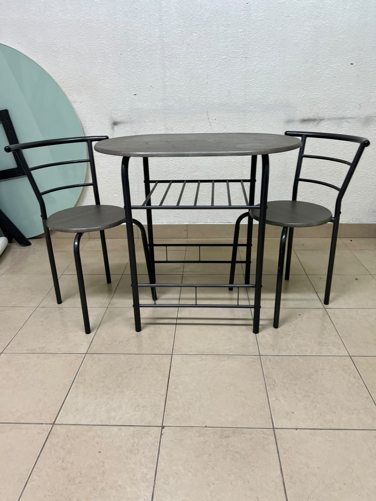 Two chairs and a table featuring an oval grey tabletop, a black tubular steel frame, and built-in storage shelves.