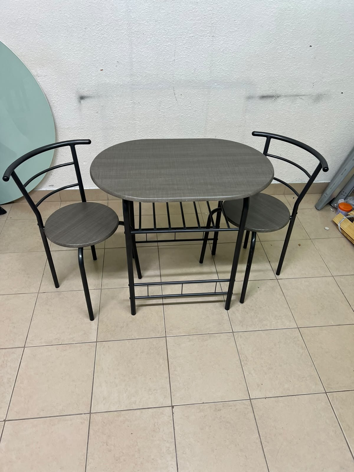 Two chairs and a table featuring an oval grey tabletop, a black tubular steel frame, and built-in storage shelves. - Image 8