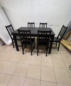 A dark solid wood dining table with matching slat-back chairs, featuring the design of the "Nordviken" collection from IKEA.