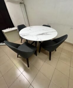 This modern dining set features a round table with a white marble-effect top, paired with curved, arm-equipped chairs upholstered in dark gray and supported by black metal legs.