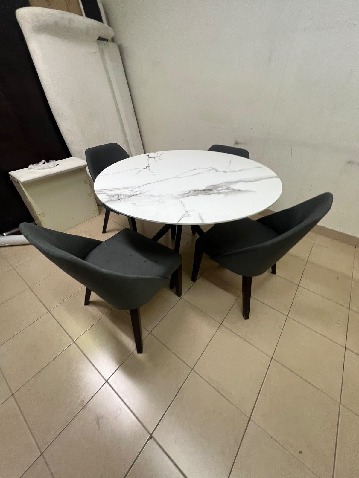 This modern dining set features a round table with a white marble-effect top, paired with curved, arm-equipped chairs upholstered in dark gray and supported by black metal legs.