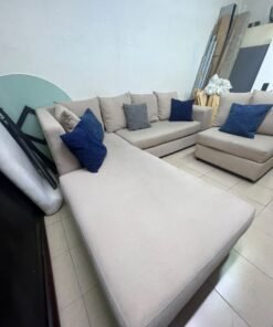 A modern L-shaped corner sofa upholstered in beige fabric, paired with a distinctive standalone lounge chair and accented with contrasting throw pillows in dark blue and patterned gray. - Image 2