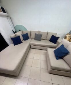 A modern L-shaped corner sofa upholstered in beige fabric, paired with a distinctive standalone lounge chair and accented with contrasting throw pillows in dark blue and patterned gray. - Image 3
