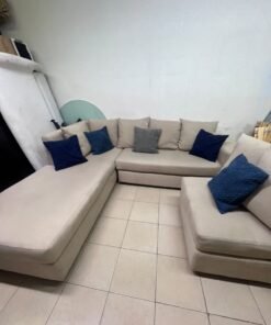 A modern L-shaped corner sofa upholstered in beige fabric, paired with a distinctive standalone lounge chair and accented with contrasting throw pillows in dark blue and patterned gray. - Image 4